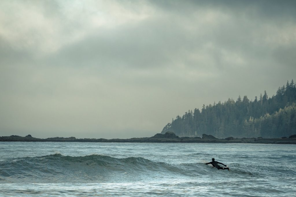 A surfer paddling out over the waves in overcast